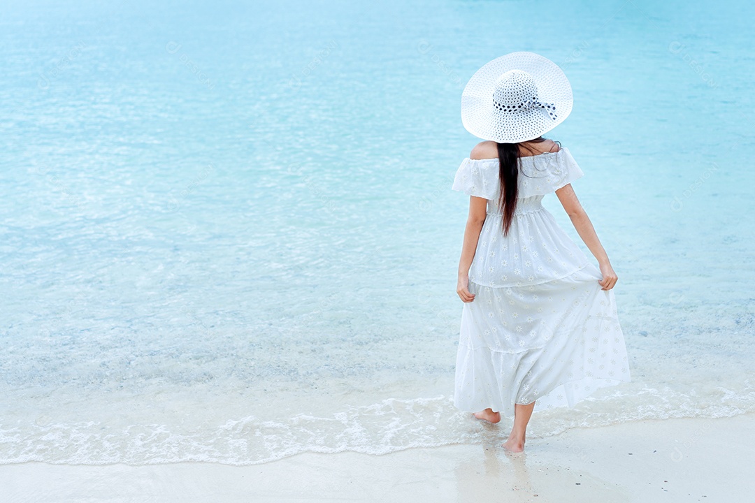 Mulher solteira andando na praia com vestido branco