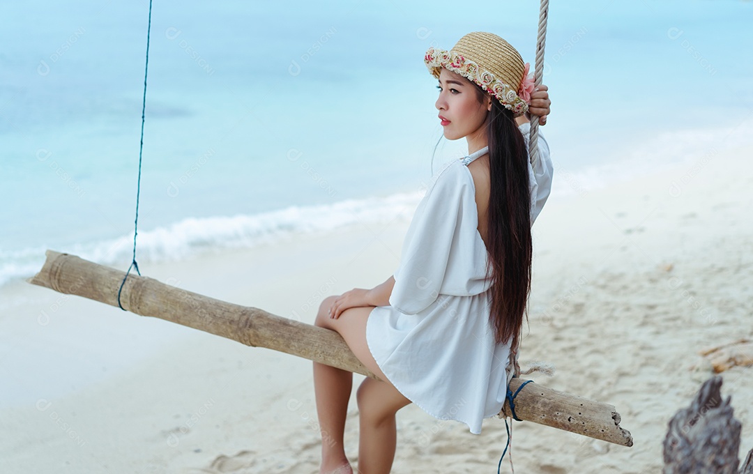 Mulher bonita asiática balançando na praia com vestido branco