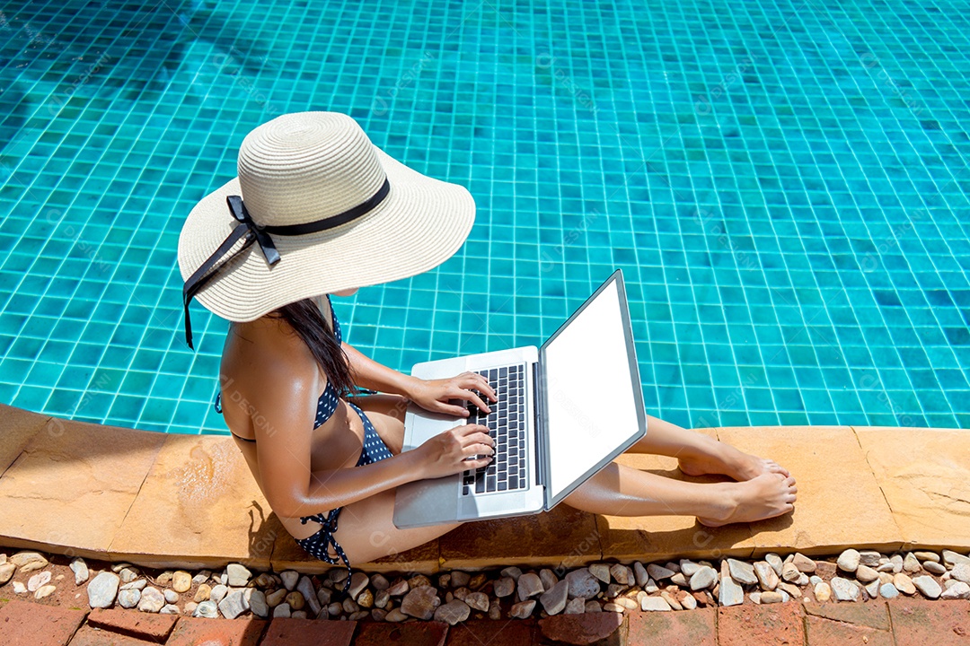 Mulher usando laptop na piscina na borda do resort com chapéu