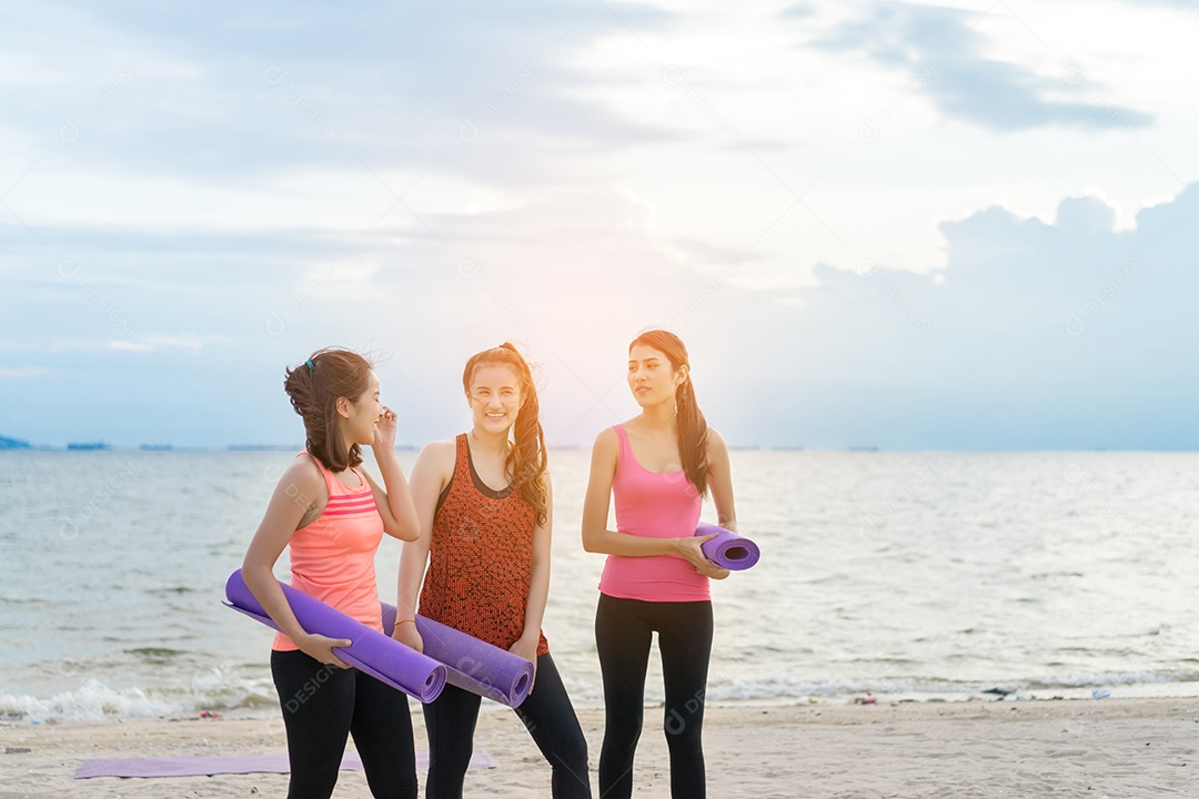 Grupo de jovens asiáticas com tapete de ioga na praia