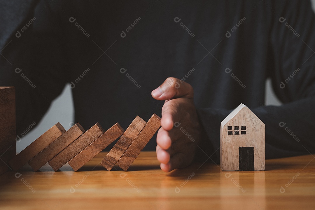 Mão parando o efeito de crise de dominó em casa segura ou plano de risco proteção imobiliária