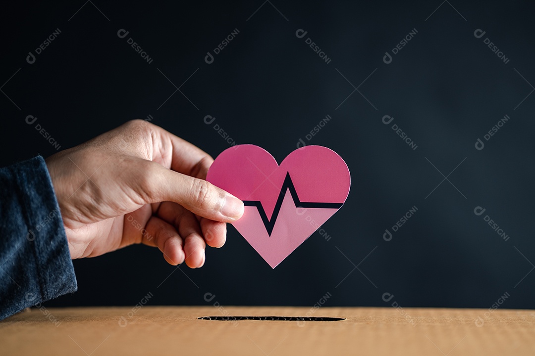 As mãos soltam o coração vermelho na caixa de doação.