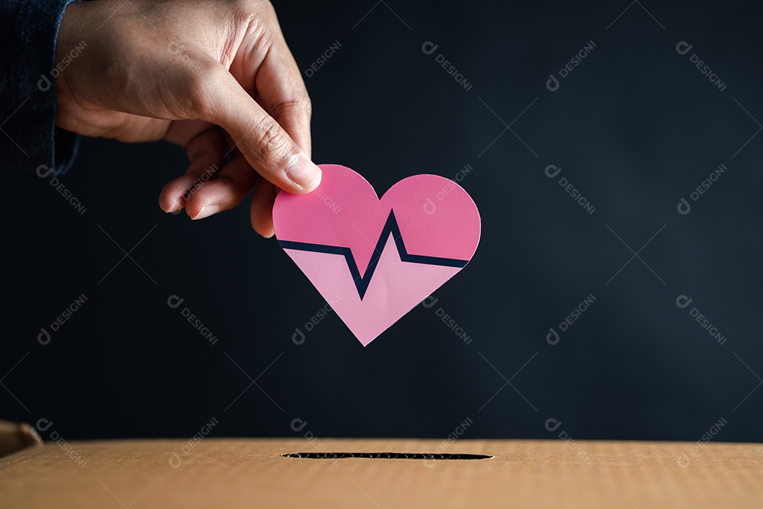 As mãos soltam o coração vermelho na caixa de doação.