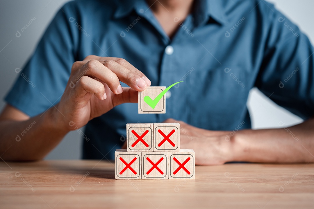 Empresário empilhando ícone verde correto que entre o ícone errado no bloco de madeira