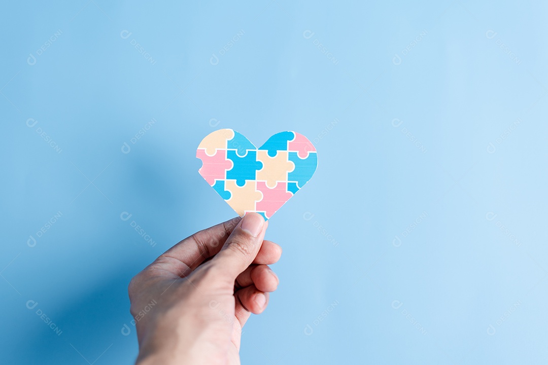 Mão segurando o quebra-cabeça do coração da consciência, símbolo de quebra-cabeça colorido de conscientização para o apoio à família do transtorno do espectro do autismo.