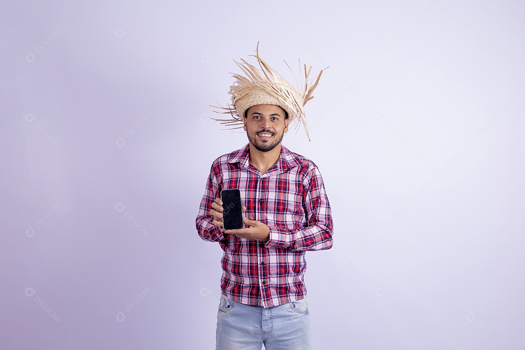 Homem jovem barbudo fantasiado celebrando festas juninas segurando celular