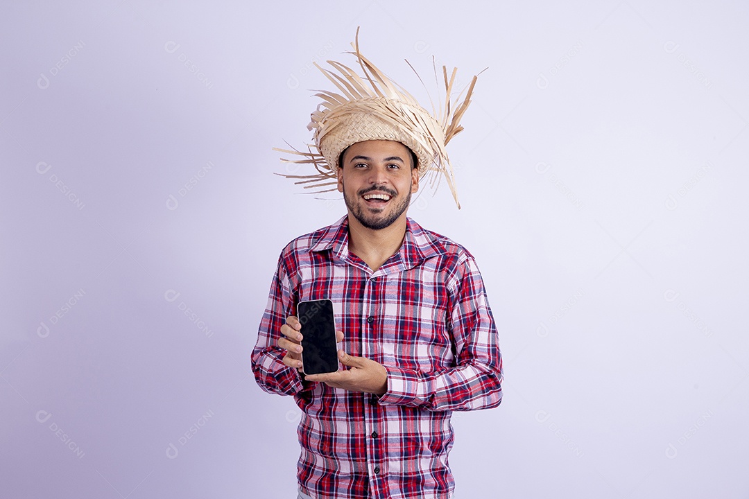 Homem jovem barbudo fantasiado celebrando festas juninas segurando celular