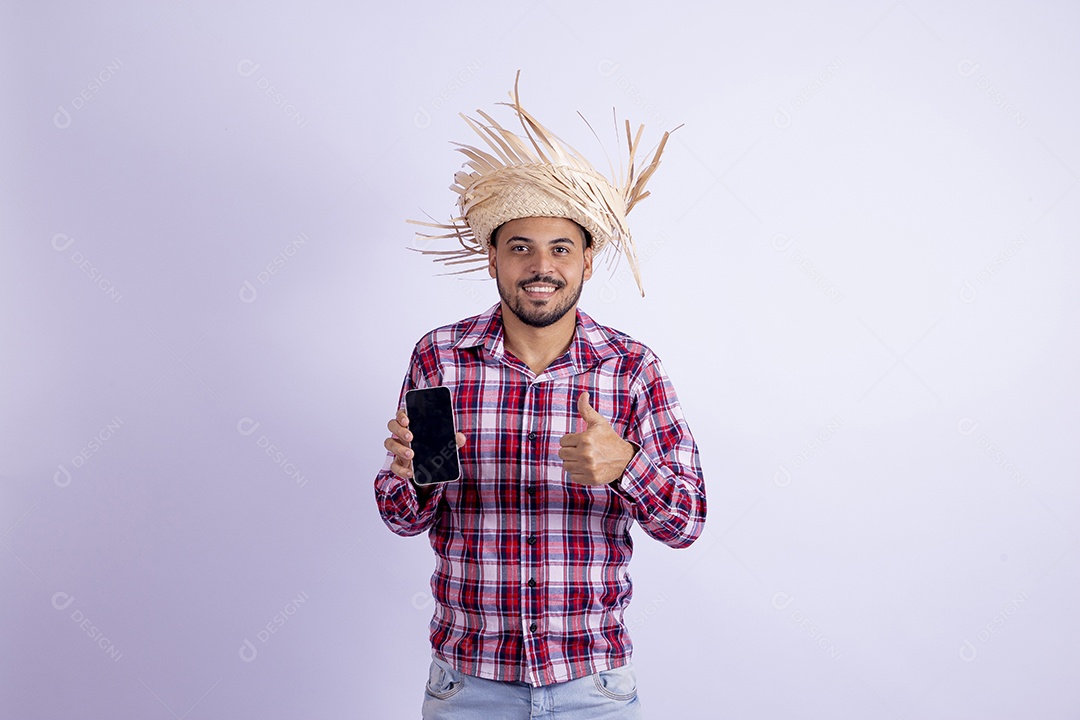 Homem jovem barbudo fantasiado celebrando festas juninas segurando celular