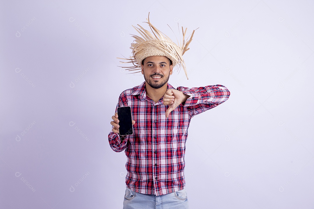 Homem jovem barbudo fantasiado celebrando festas juninas segurando celular