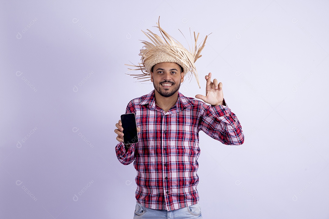 Homem jovem barbudo fantasiado celebrando festas juninas segurando celular