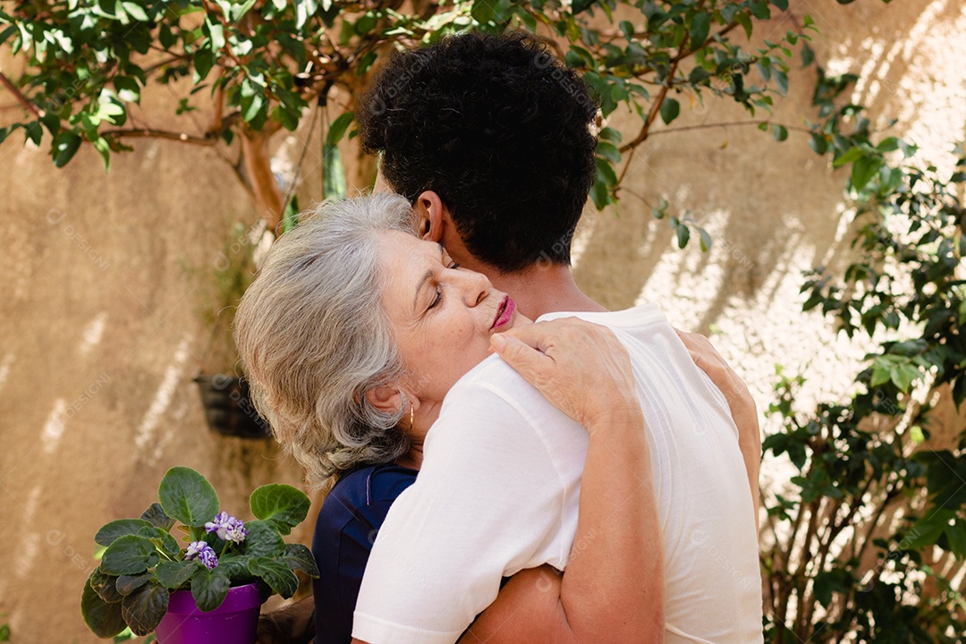 Mãe caucasiana e seu filho negro no jardim da casa. Família inter-racial feliz.