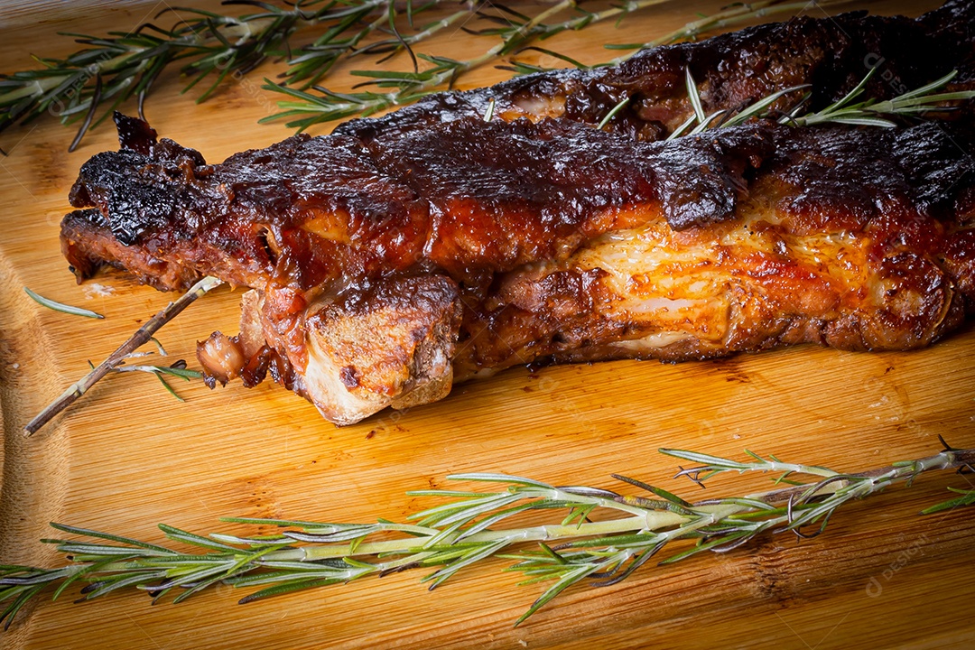 Costelinha de porco assada com molho barbecue de alecrim em uma tábua de madeira. Visão de perspectiva.