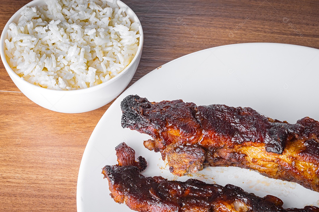 Costelinha suína assada com molho barbecue, arroz e refrigerante de guaraná em porcelana branca. Mesa de madeira. Fechar vista.