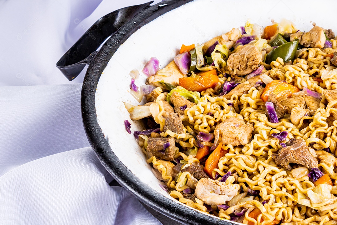 Yakisoba japonês com macarrão frito em panela metálica branca na mesa com toalha de mesa branca e fundo preto, com pauzinhos de comida japonesa... Close view.