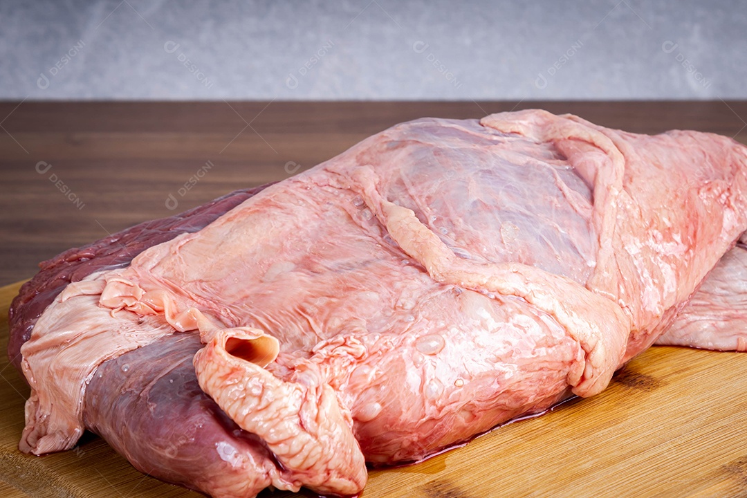 Carne para churrasco. Carne crua coberta de gordura em uma placa de madeira sobre um fundo de madeira. Temperei com coentro, alho e tomate