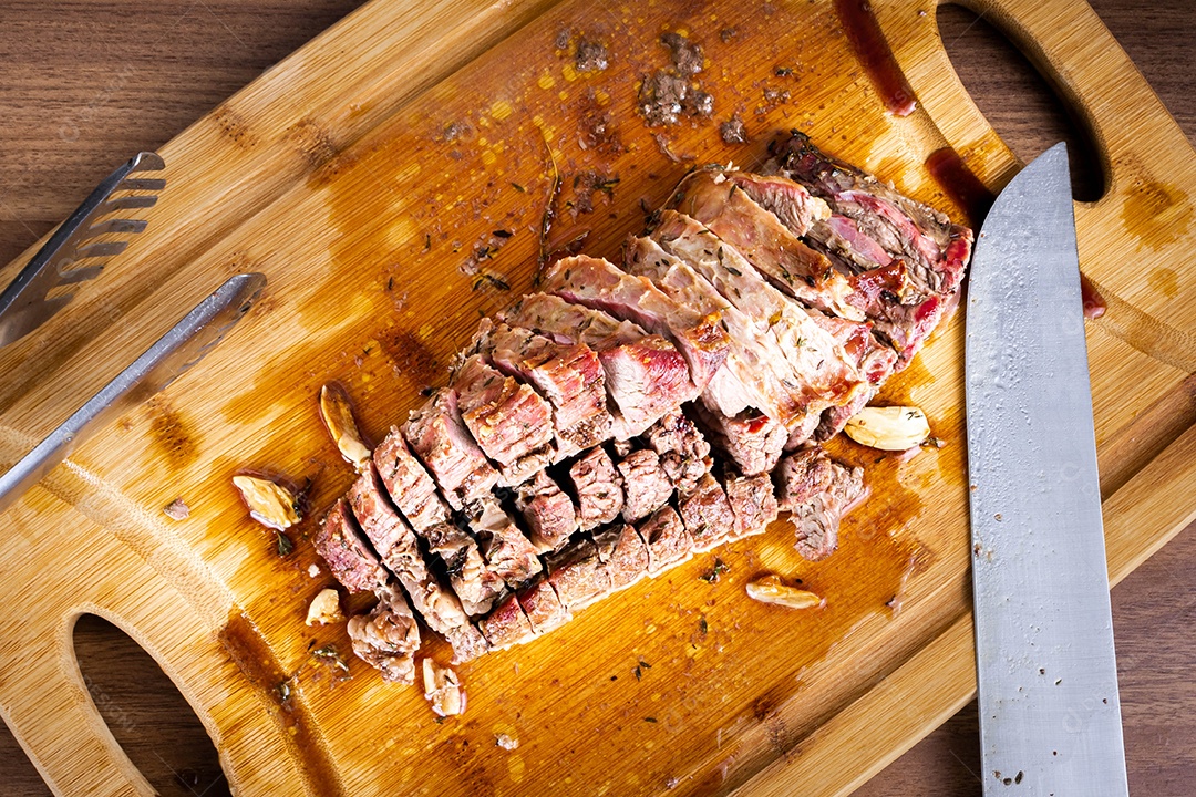 Carne para churrasco. Carne assada com batatas e tomilho numa tábua de madeira, totalmente cortada às rodelas. Vista do topo.