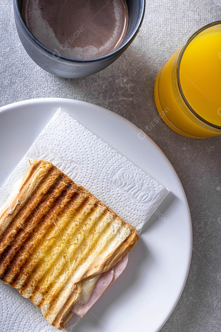 Misto quente. Sanduíche com queijo e presunto na grelha. Servido em toalha xadrez. Acompanha suco de laranja. Visão de perspectiva.