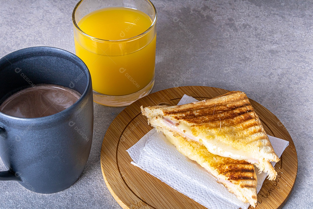 Misto quente. Sanduíche com queijo e presunto na grelha. Servido em toalha xadrez. Acompanha suco de laranja. Visão de perspectiva.