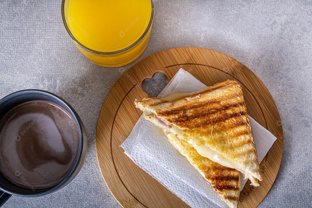 Misto quente. Sanduíche com queijo e presunto na grelha. Servido em toalha xadrez. Acompanha suco de laranja. Visão de perspectiva.