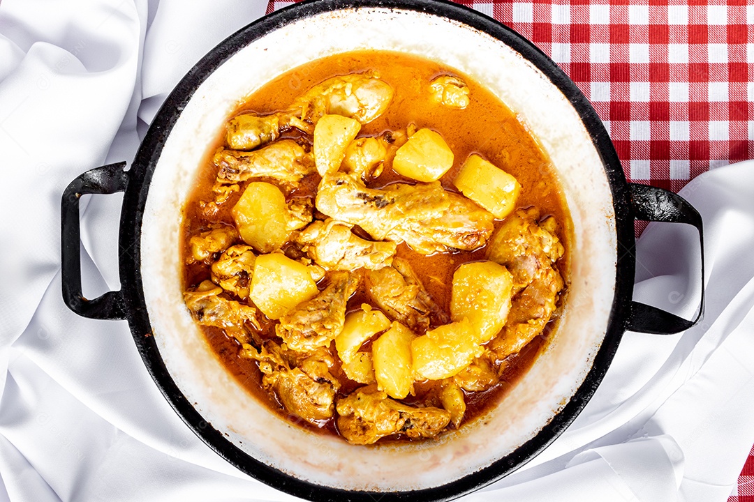 Ensopado de frango caseiro com tomate, cebola e batata na mesa de tecido preto e prato com arroz