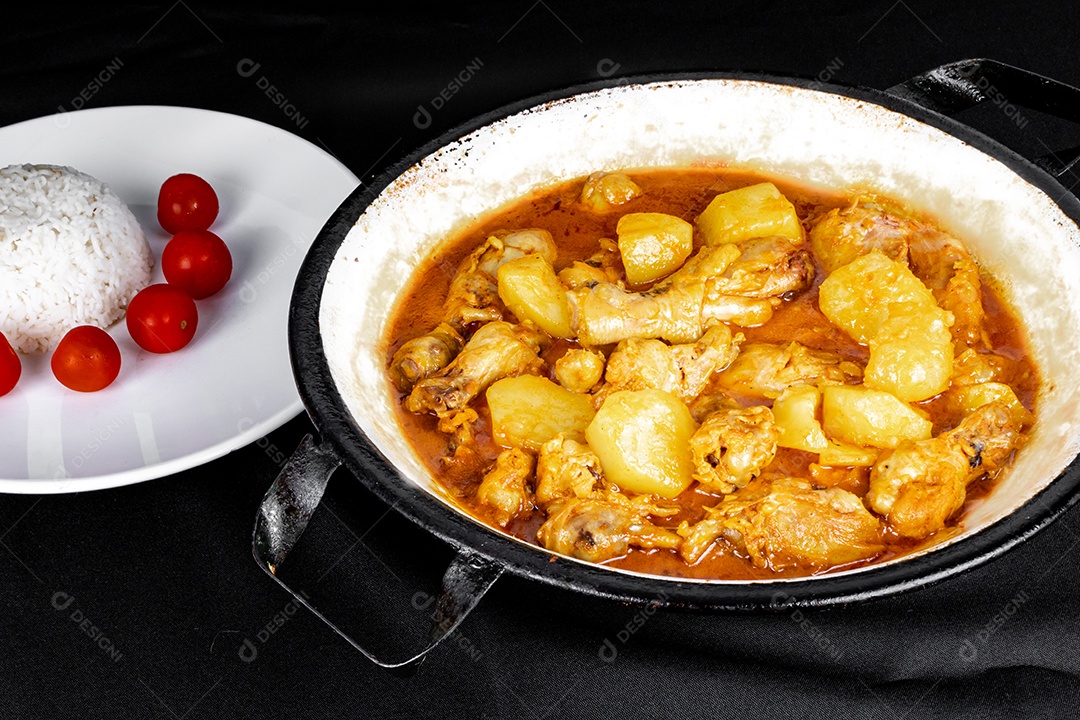 Ensopado de frango caseiro com tomate, cebola e batata na mesa de tecido preto e prato com arroz