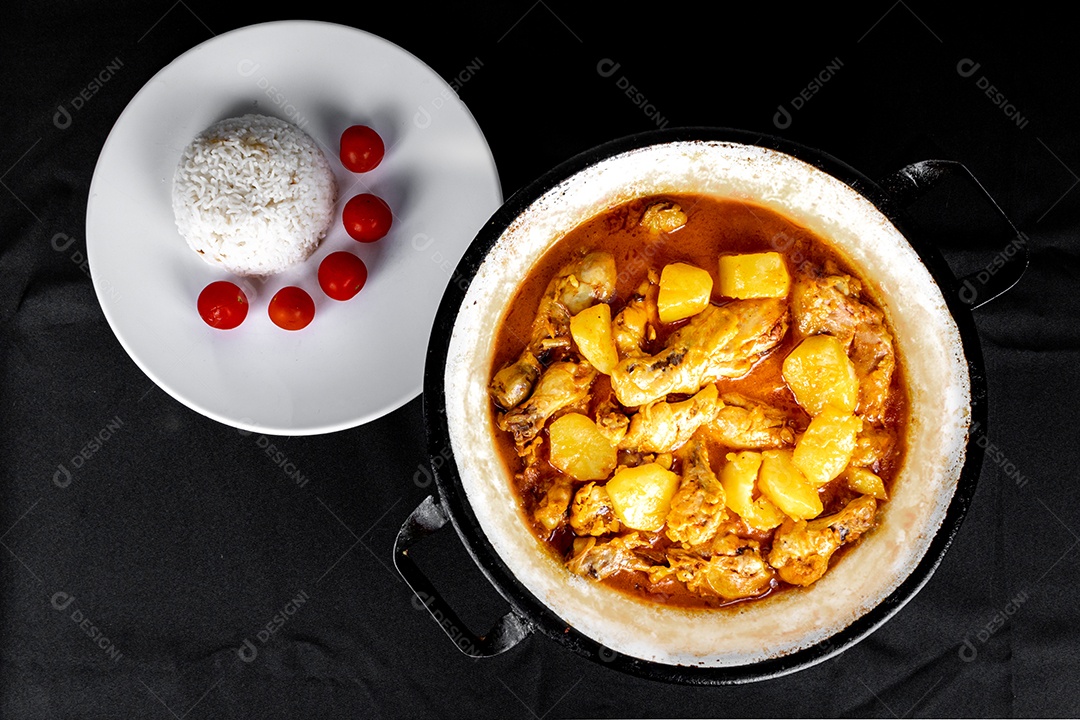 Homemade chicken stew with tomato, onion and potato on black fabric table and plate with rice