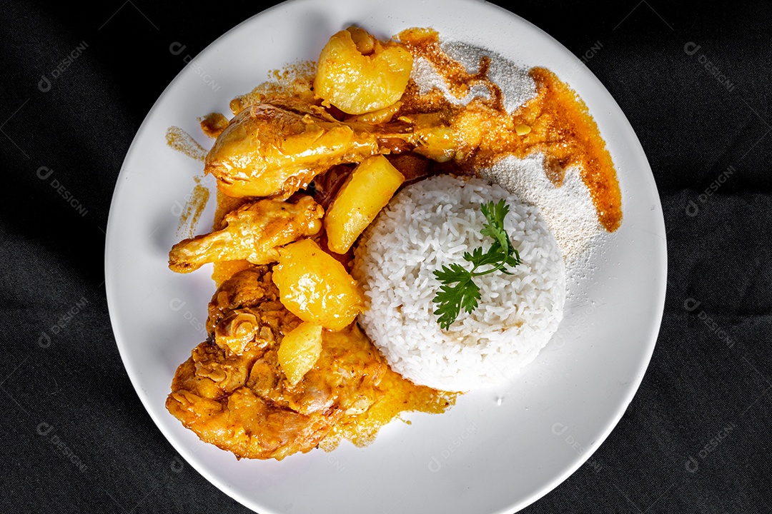 Ensopado de frango caseiro com tomate, cebola e batata em uma mesa de tecido preto e prato com arroz, feijão e suco de laranja. Vista do topo.