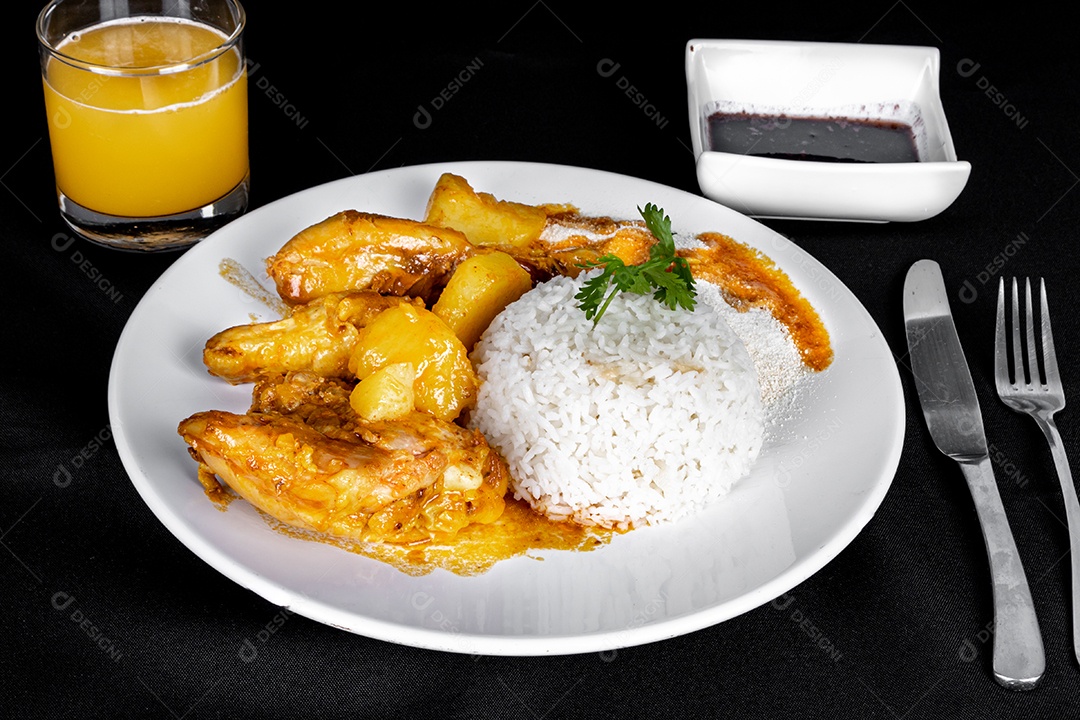 Ensopado de frango caseiro com tomate, cebola e batata em uma mesa de tecido preto e prato com arroz, feijão e suco de laranja. Vista do topo.