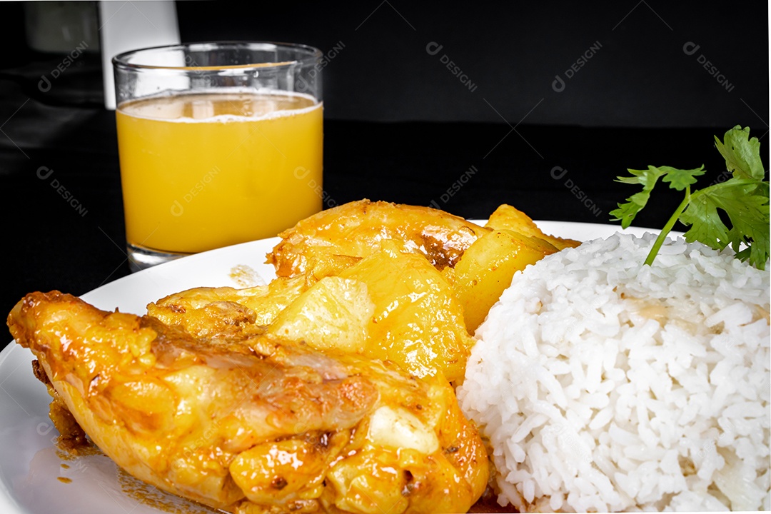 Ensopado de frango caseiro com tomate, cebola e batata em uma mesa de tecido preto e prato com arroz, feijão e suco de laranja. Vista do topo.