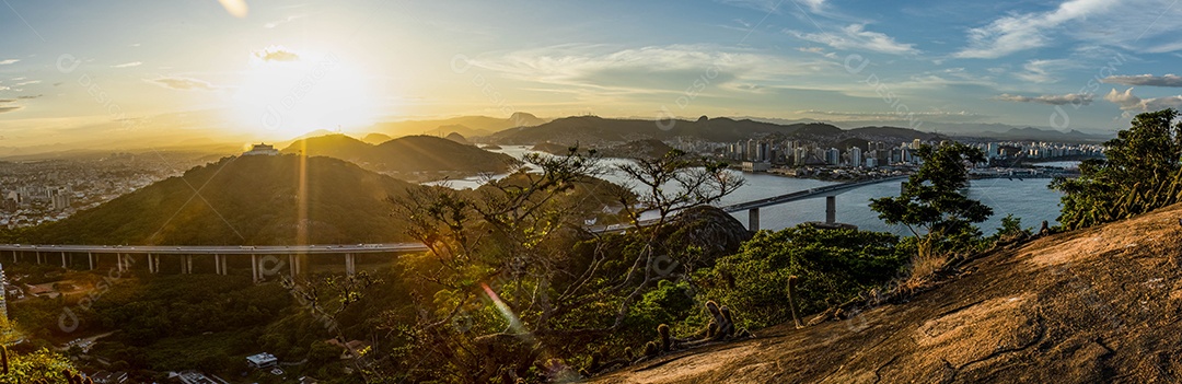 Fotografia do Convento da Penha ao entardecer, mostrando também as cidades de Vila Velha, Vitória e Terceira Ponte.