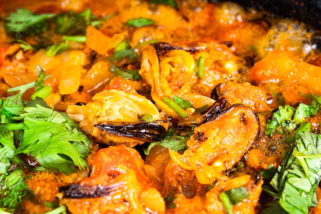 Deliciosa moqueca de peixe brasileiro com tomate, cebola, azeite, coentro e semente de orocum. Feito em panela de barro sobre mesa branca e fundo preto