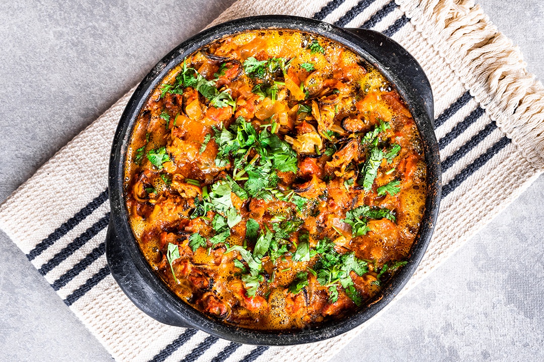Deliciosa moqueca de peixe brasileiro com tomate, cebola, azeite, coentro e semente de orocum. Feito em panela de barro sobre mesa branca e fundo preto