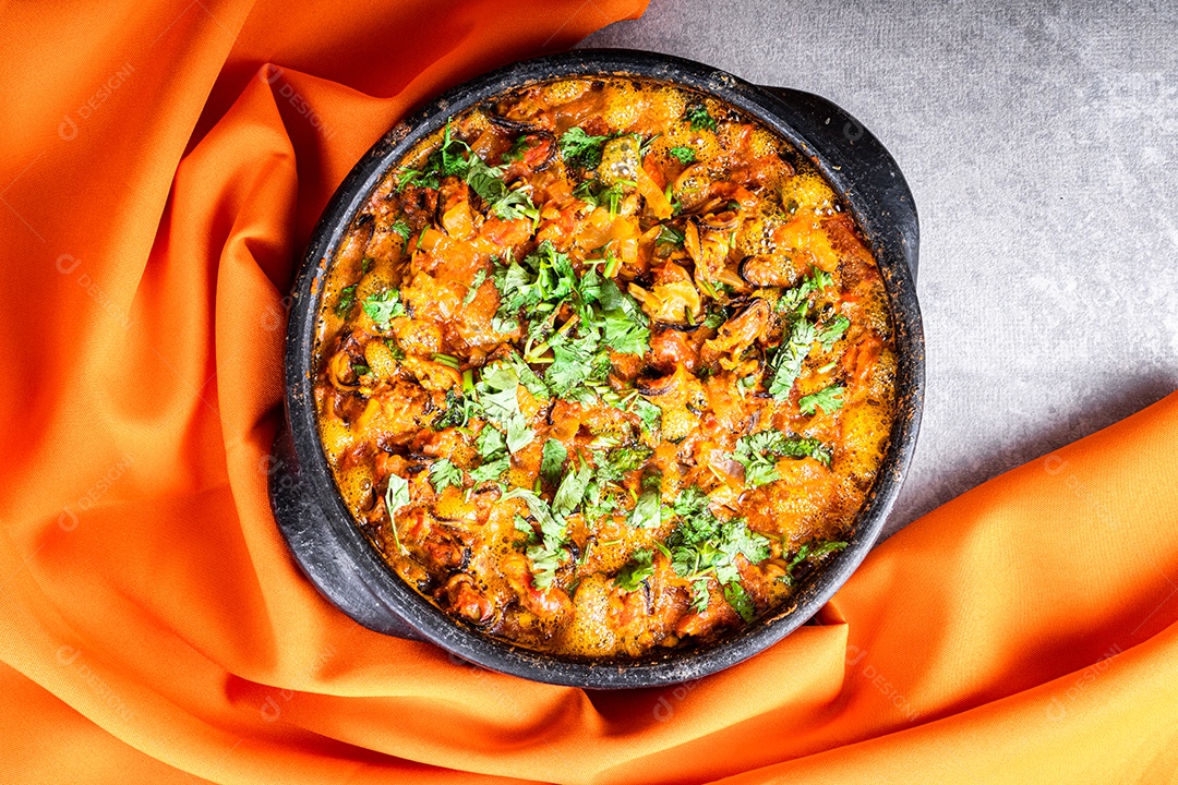 Deliciosa moqueca de peixe brasileiro com tomate, cebola, azeite, coentro e semente de orocum. Feito em panela de barro sobre mesa branca e fundo preto