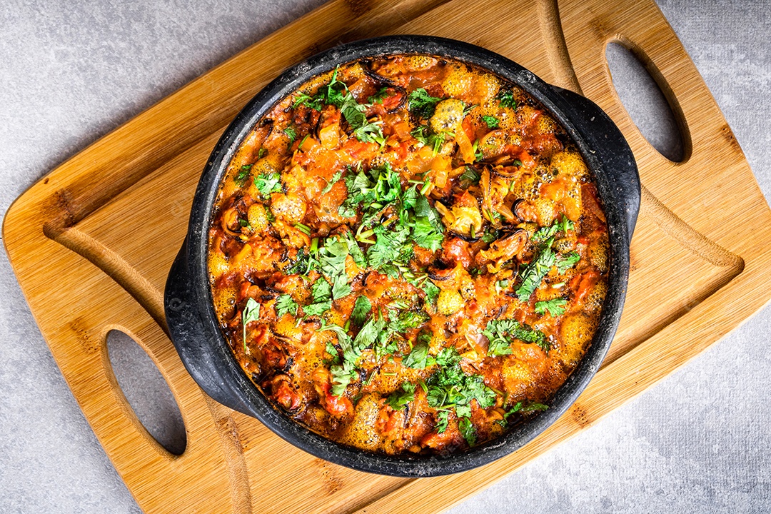 Deliciosa moqueca de peixe brasileiro com tomate, cebola, azeite, coentro e semente de orocum. Feito em panela de barro sobre mesa branca e fundo preto