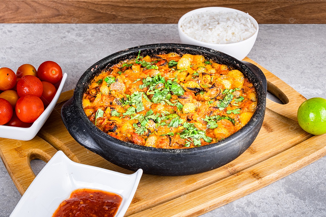 Deliciosa moqueca de peixe brasileiro com tomate, cebola, azeite, coentro e semente de orocum. Feito em panela de barro sobre mesa branca e fundo preto