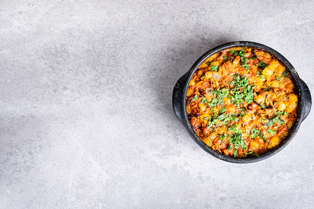 Deliciosa moqueca de peixe brasileiro com tomate, cebola, azeite, coentro e semente de orocum. Feito em panela de barro sobre mesa branca e fundo preto