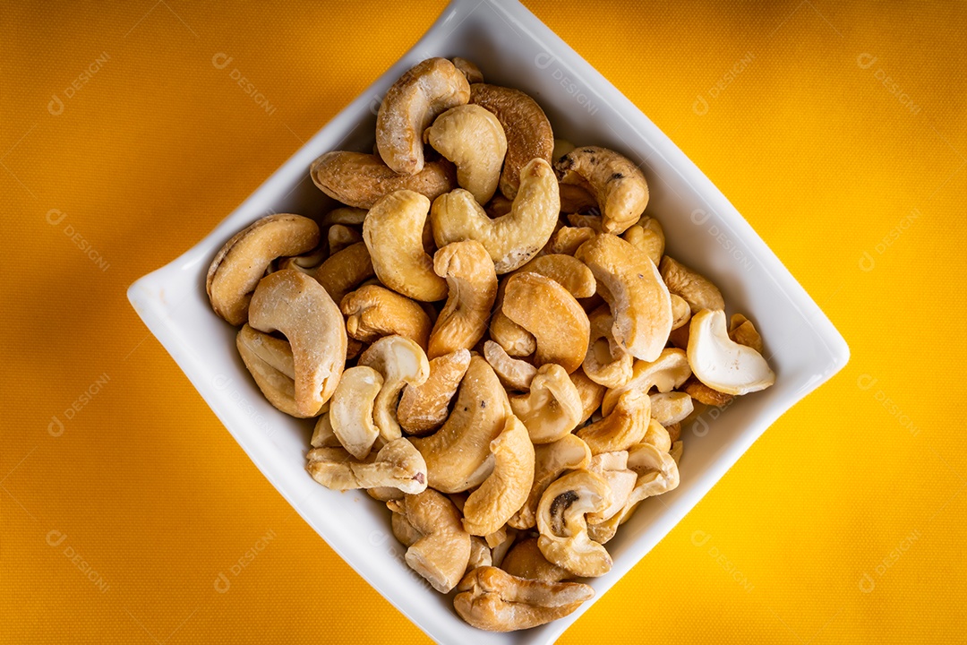 Castanha de caju em pote de louça em fundo branco. Vista do topo.