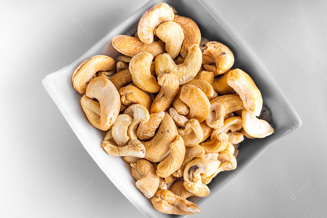 Castanha de caju em pote de louça em fundo branco. Vista do topo.