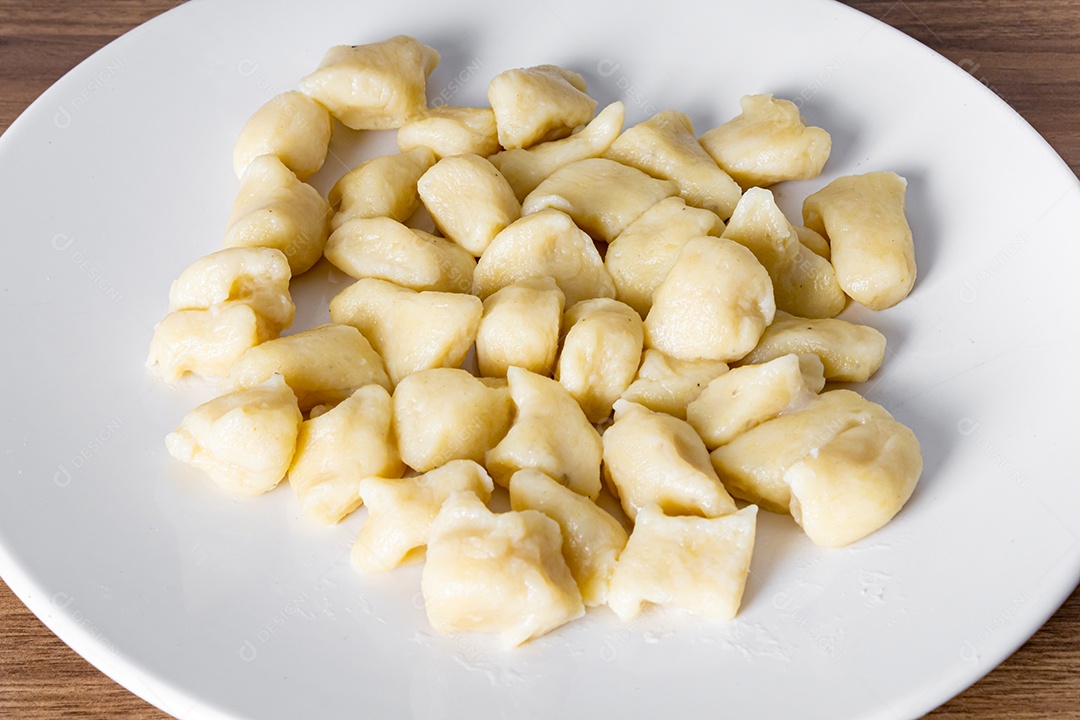 Gnocc assado em uma placa branca em um fundo de madeira. detalhe da manjericão e dos tomates pequenos. com forquilha e toalha descascada na mesa.