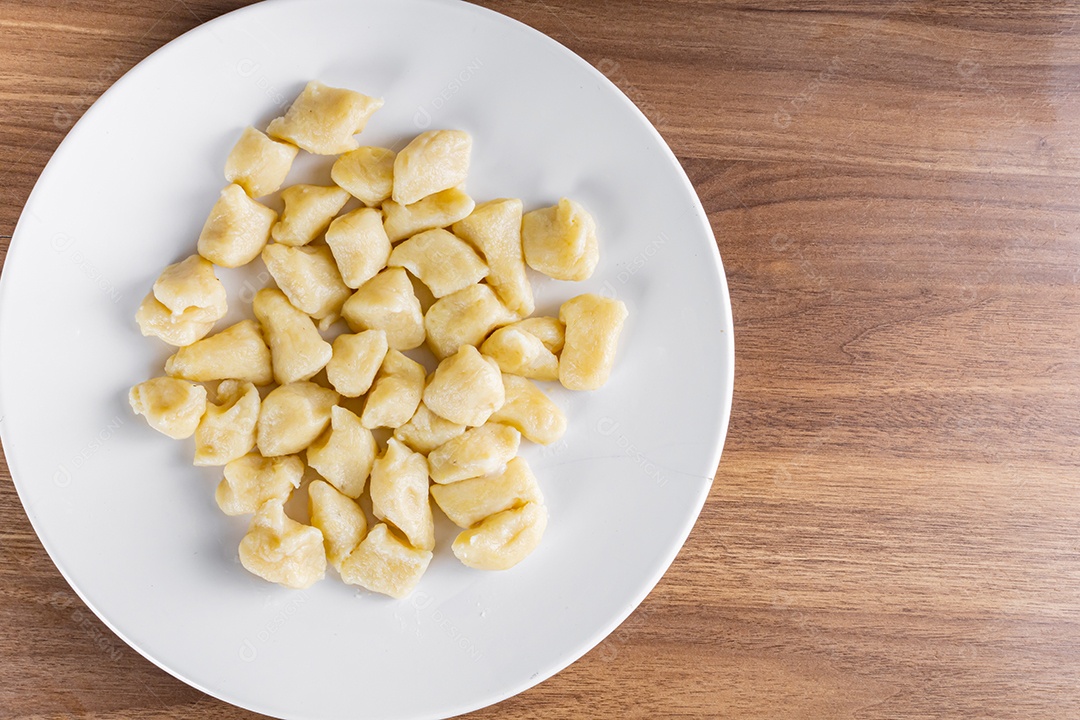 Gnocc assado em uma placa branca em um fundo de madeira. detalhe da manjericão e dos tomates pequenos. com forquilha e toalha descascada na mesa.