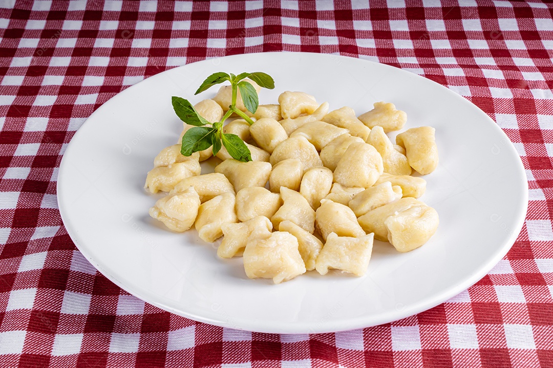 Nhocchi cozido com carne moída ao molho de tomate, coberto por queijo ralado, montado em travessa de vidro.