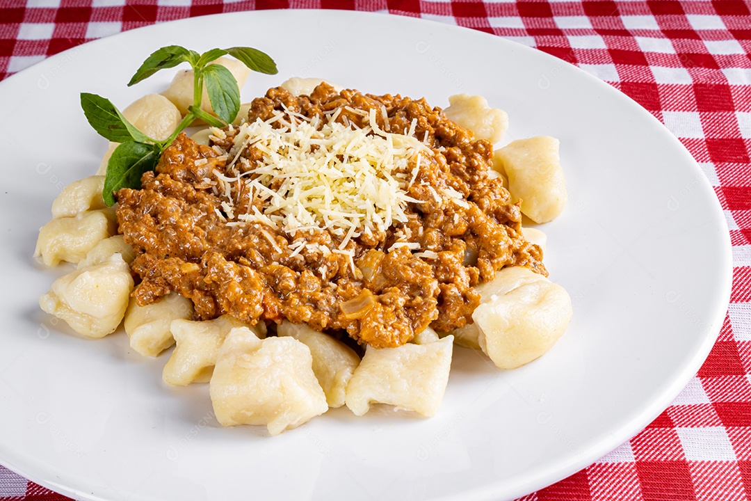Nhocchi cozido com carne moída ao molho de tomate, coberto por queijo ralado, montado em travessa de vidro.