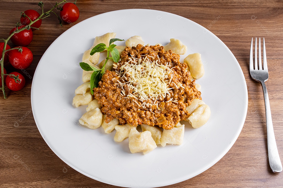 Nhocchi cozido com carne moída ao molho de tomate, coberto por queijo ralado, montado em travessa de vidro.