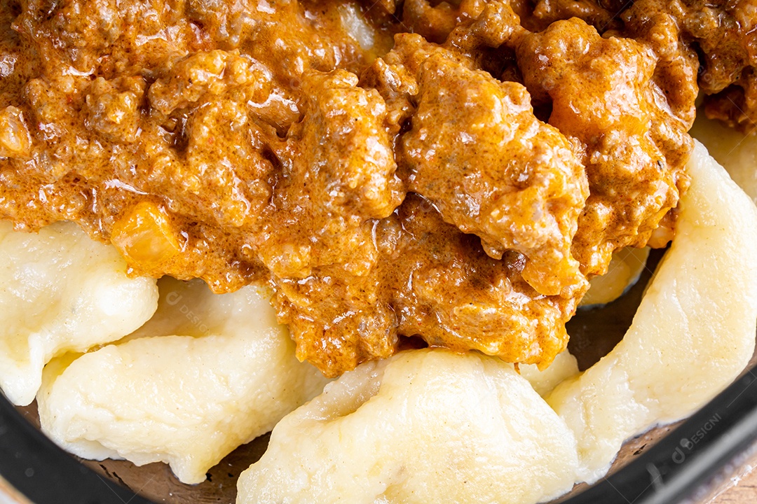 Nhocchi cozido com carne moída ao molho de tomate, coberto por queijo ralado, montado em travessa de vidro.