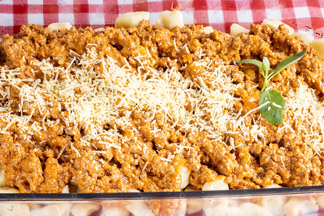 Nhocchi cozido com carne moída ao molho de tomate, coberto por queijo ralado, montado em travessa de vidro.