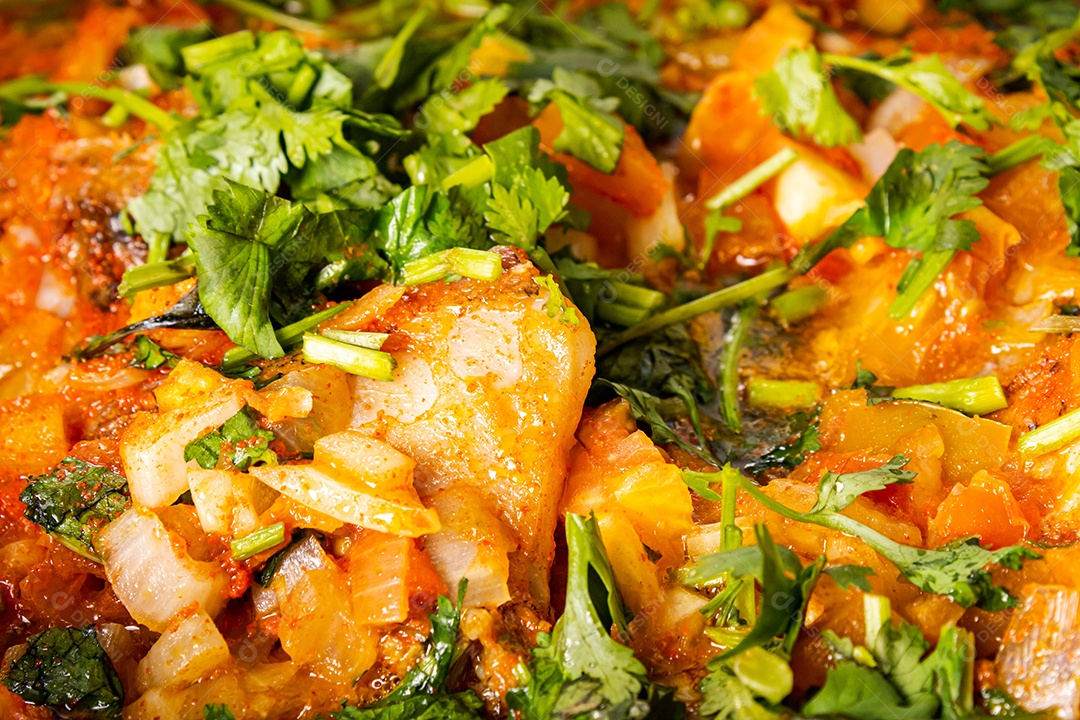 Deliciosa moqueca de peixe brasileiro com tomate, cebola, azeite, coentro e semente de orocum. Feito em panela de barro sobre mesa branca e fundo preto. Com arroz.