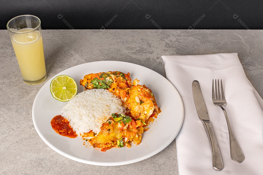 Deliciosa moqueca de peixe brasileiro com tomate, cebola, azeite, coentro e semente de orocum. Servido em prato de porcelana branca com arroz. Com toalha laranja ao redor.