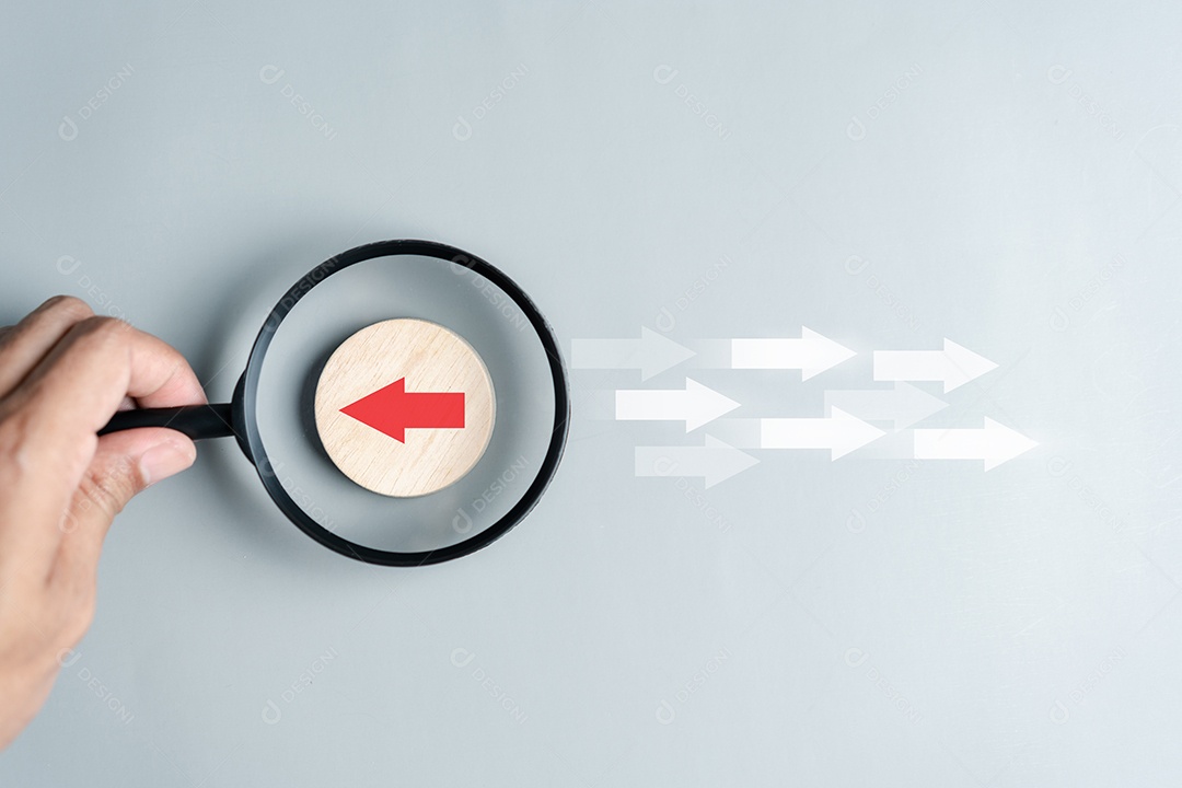 Mão segurando lupa foco para seta vermelha e direção diferente voltada para a direção oposta
