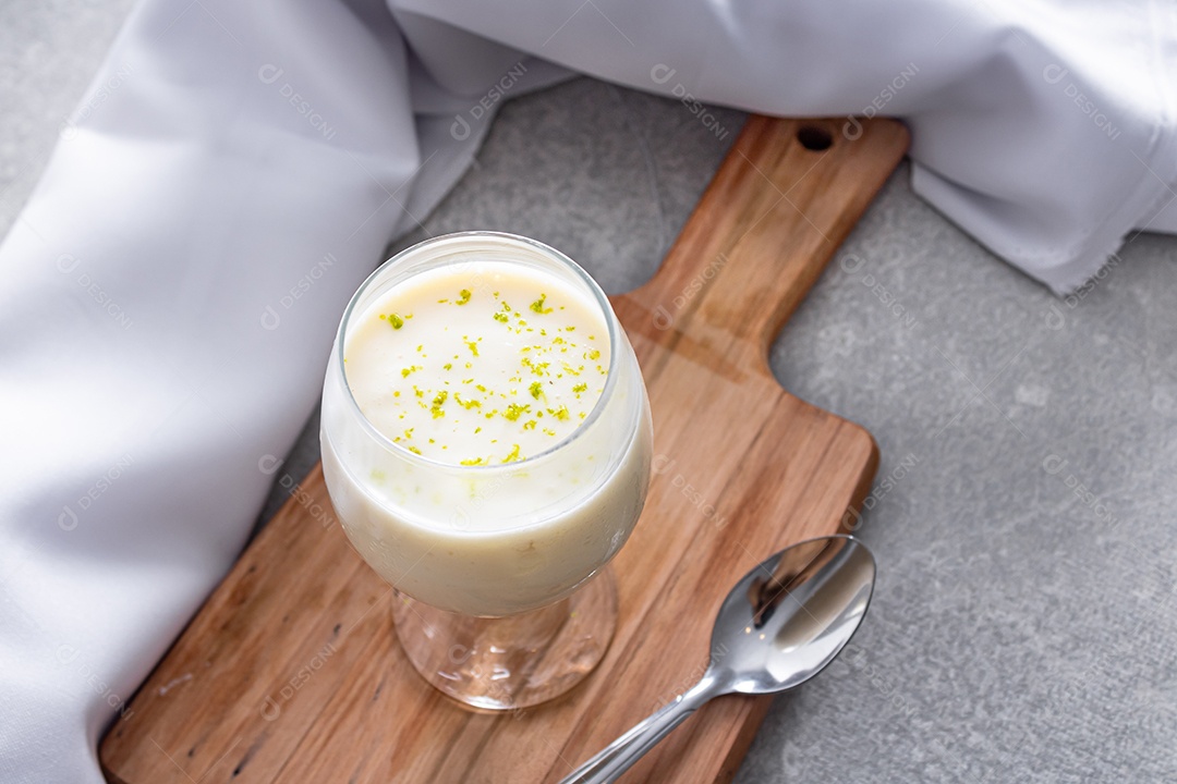 Deliciosa mousse de limão sobre uma tábua de madeira e um fundo de mesa branco, com uma toalha branca em volta e uma colher de metal
