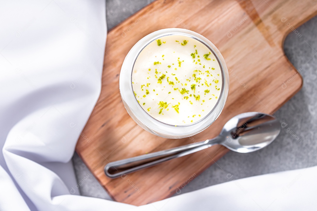Deliciosa mousse de limão sobre uma tábua de madeira e um fundo de mesa branco, com uma toalha branca em volta e uma colher de metal